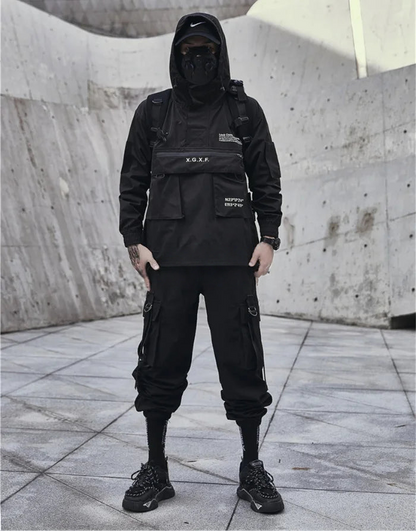 Person wearing a black tactical outfit with a hood in an urban setting.